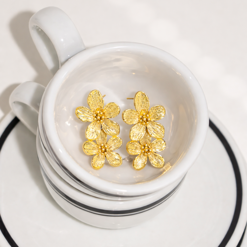 Two pairs of Spring Bloom EARRINGS rest inside a teacup, showing their layered gold flower design from above.