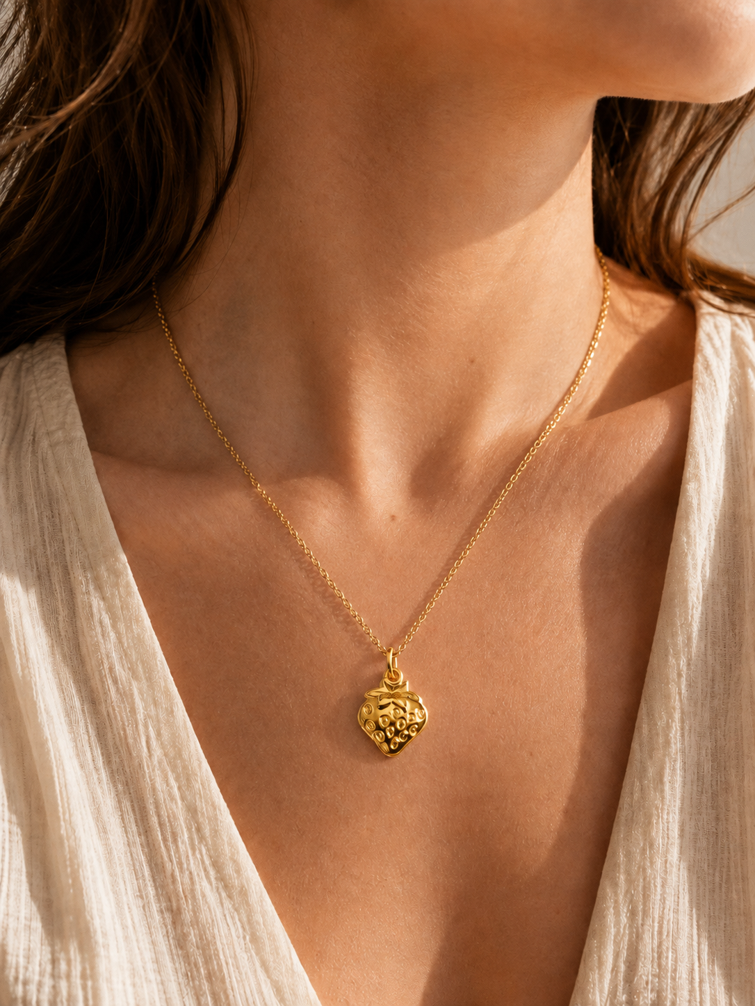The Strawberry CHARM worn on a fine gold chain at the neckline, styled with an open cream blouse in soft natural light.