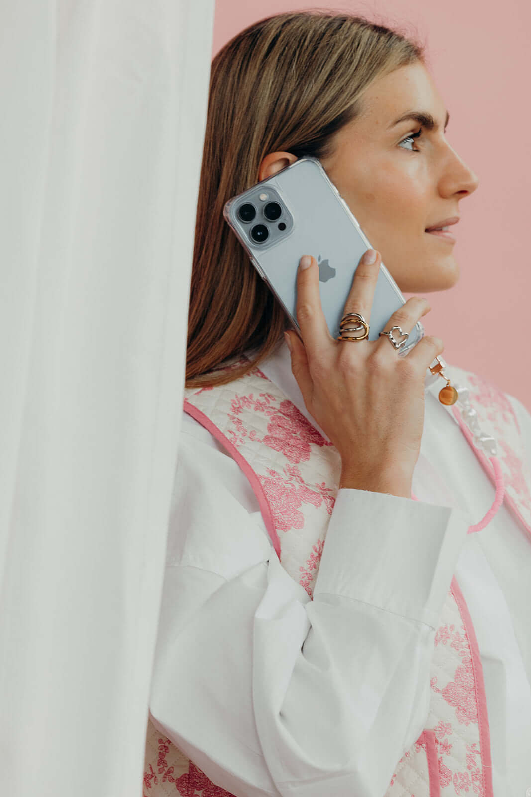 Woman on the phone wearing the silver heart-shaped Street Side RING stacked with other rings on her hand, pink backdrop.
