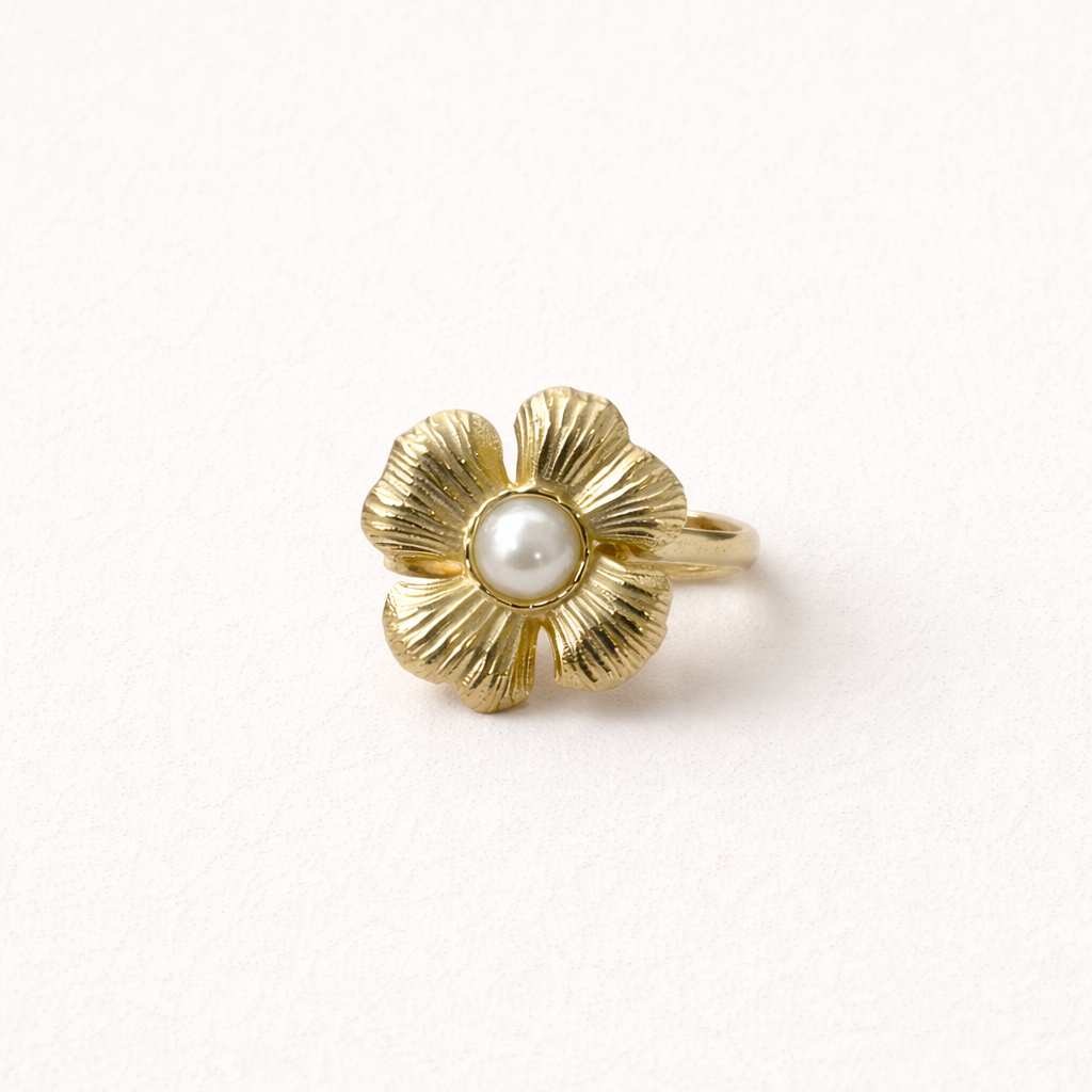 Gold ring shaped like a textured five-petal flower with a pearl center, shown at an angle on a cream backdrop — Summertime Harmony RING.