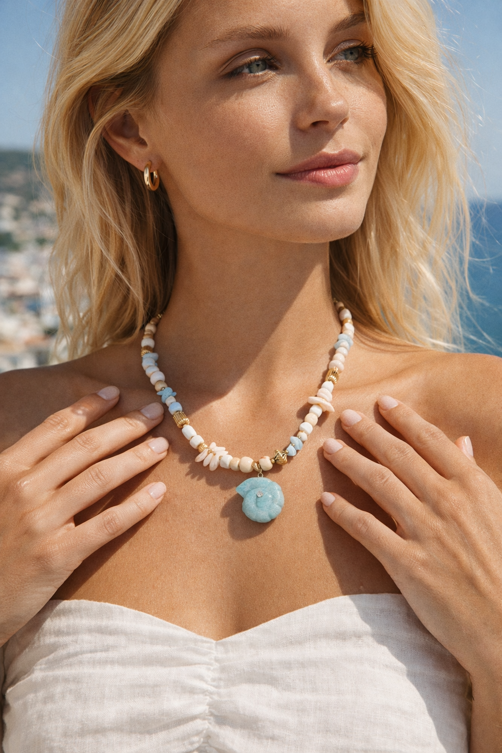 The Tahiti NECKLACE worn close-up as the model rests her hands on her chest, its carved shell pendant catching the sunlight.