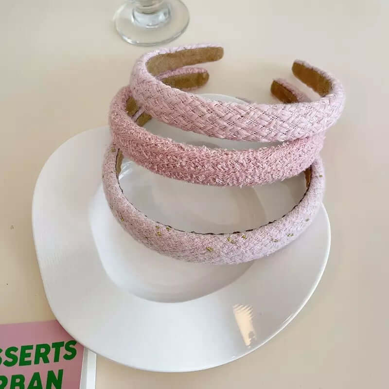 Three pink tweed and boucle headbands in different weaves stacked together on a white plate.