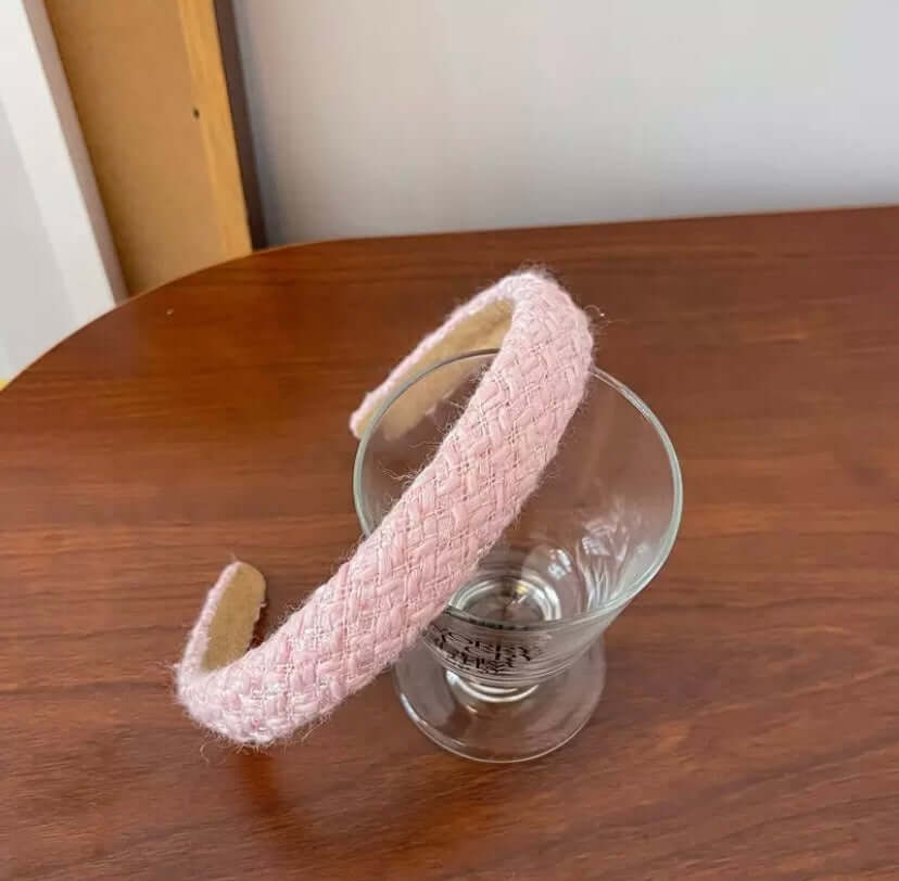 A single pink basket-weave textured headband resting on a wood table beside a glass.