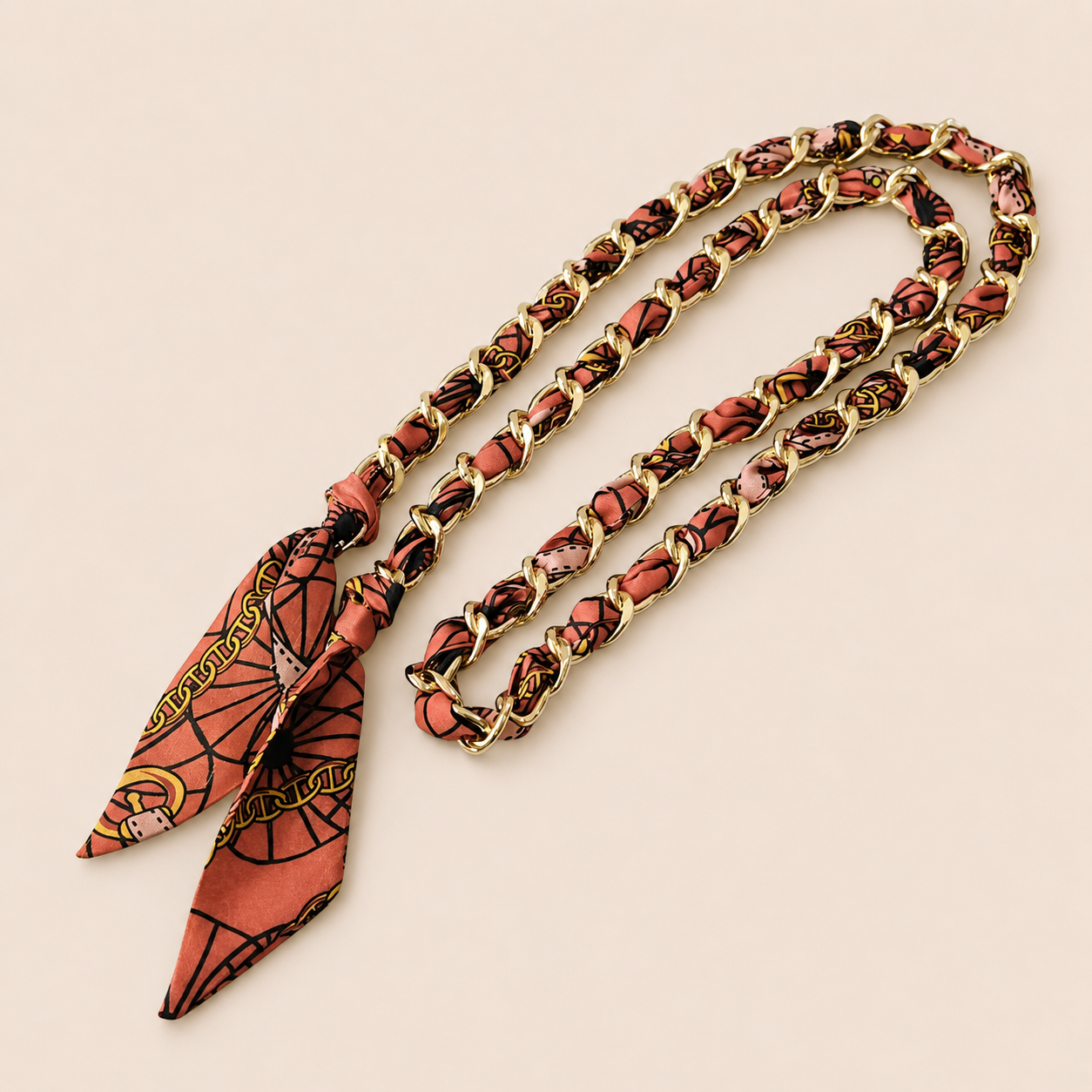 Terracotta printed silk scarf woven through a gold chain-link Tossa phone chain, tied in a knot.