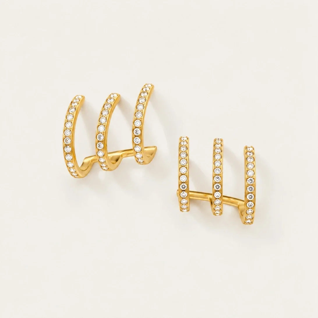 Pair of gold Triad EARRINGS with three parallel zirconia pavé bands on a cream background — Folie à Trois