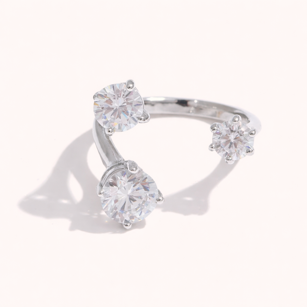 Open silver ring set with three round clear stones at different heights, shown at an angle on a cream backdrop.