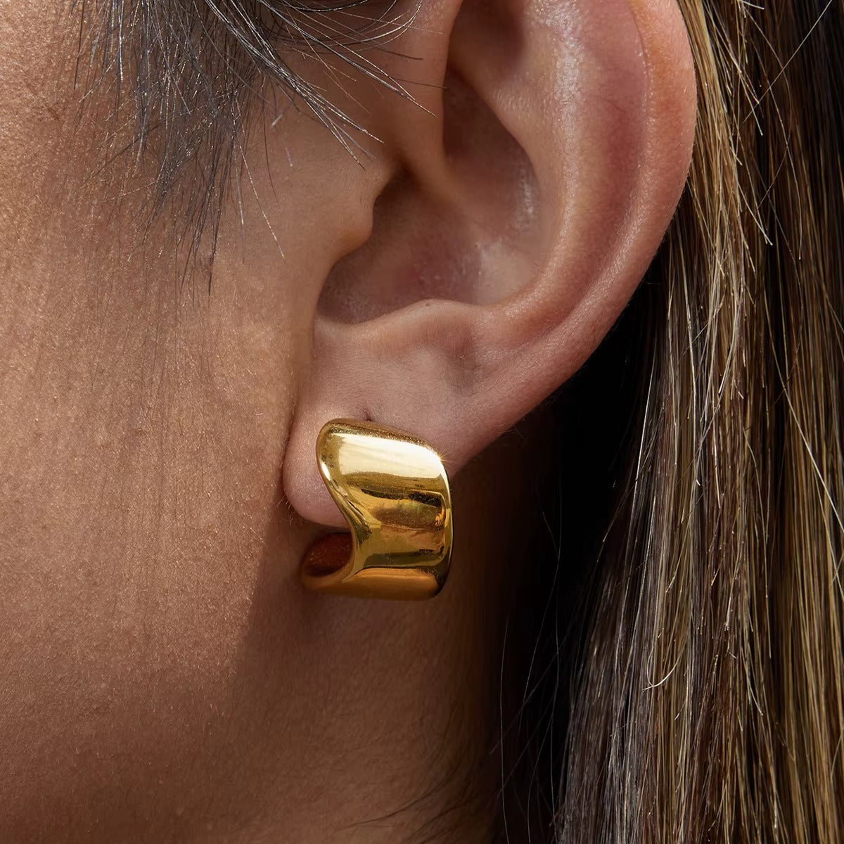 Verbier Earring worn on the ear in gold, the sculptural wave hoop catching the light up close nicely.