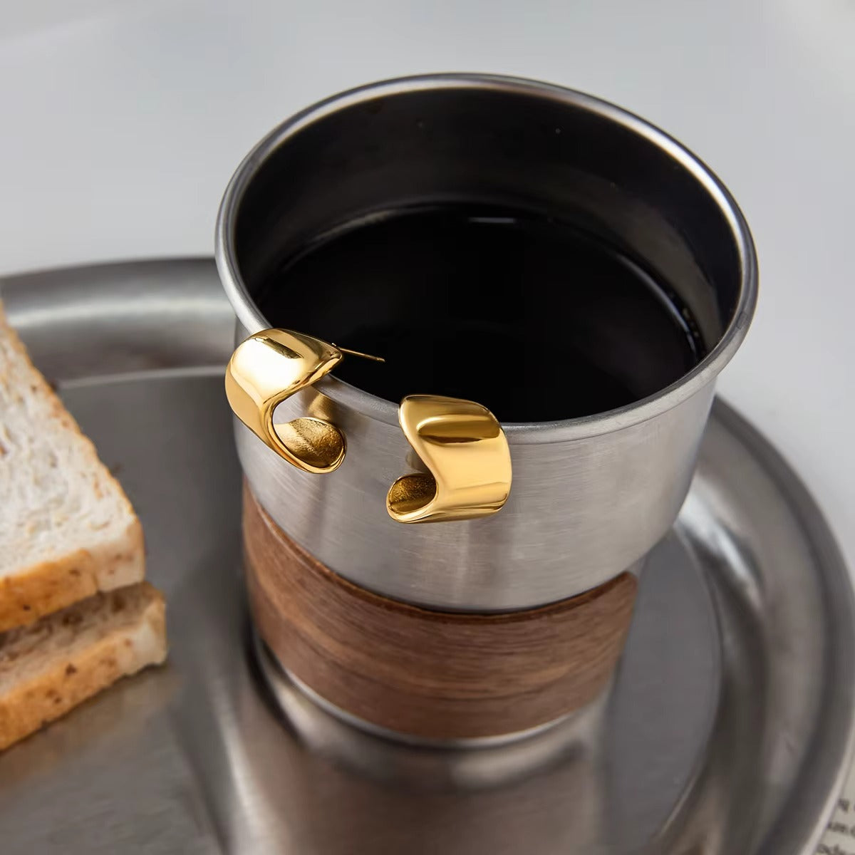 Verbier Earrings in gold hooked over the rim of a white coffee cup and resting neatly on its saucer.