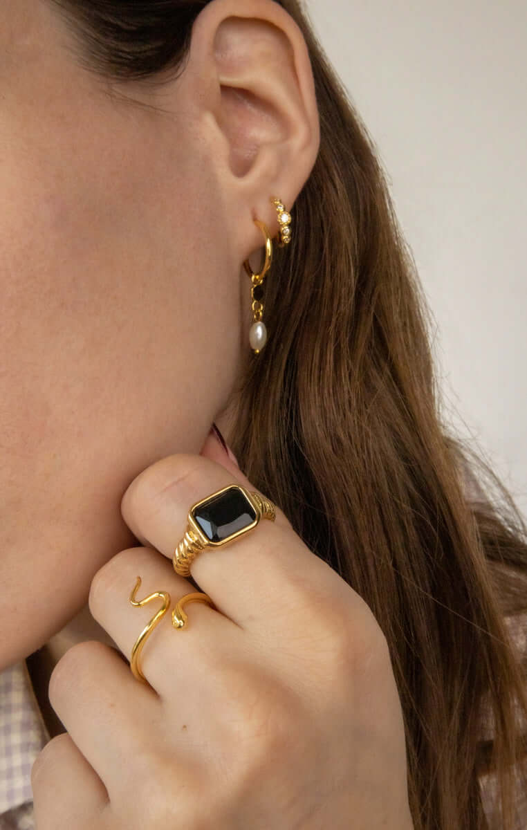 Vintage Vibes RING with black rectangular stone worn stacked with a slim gold snake-shaped ring, gold pearl hoop earring visible nearby.