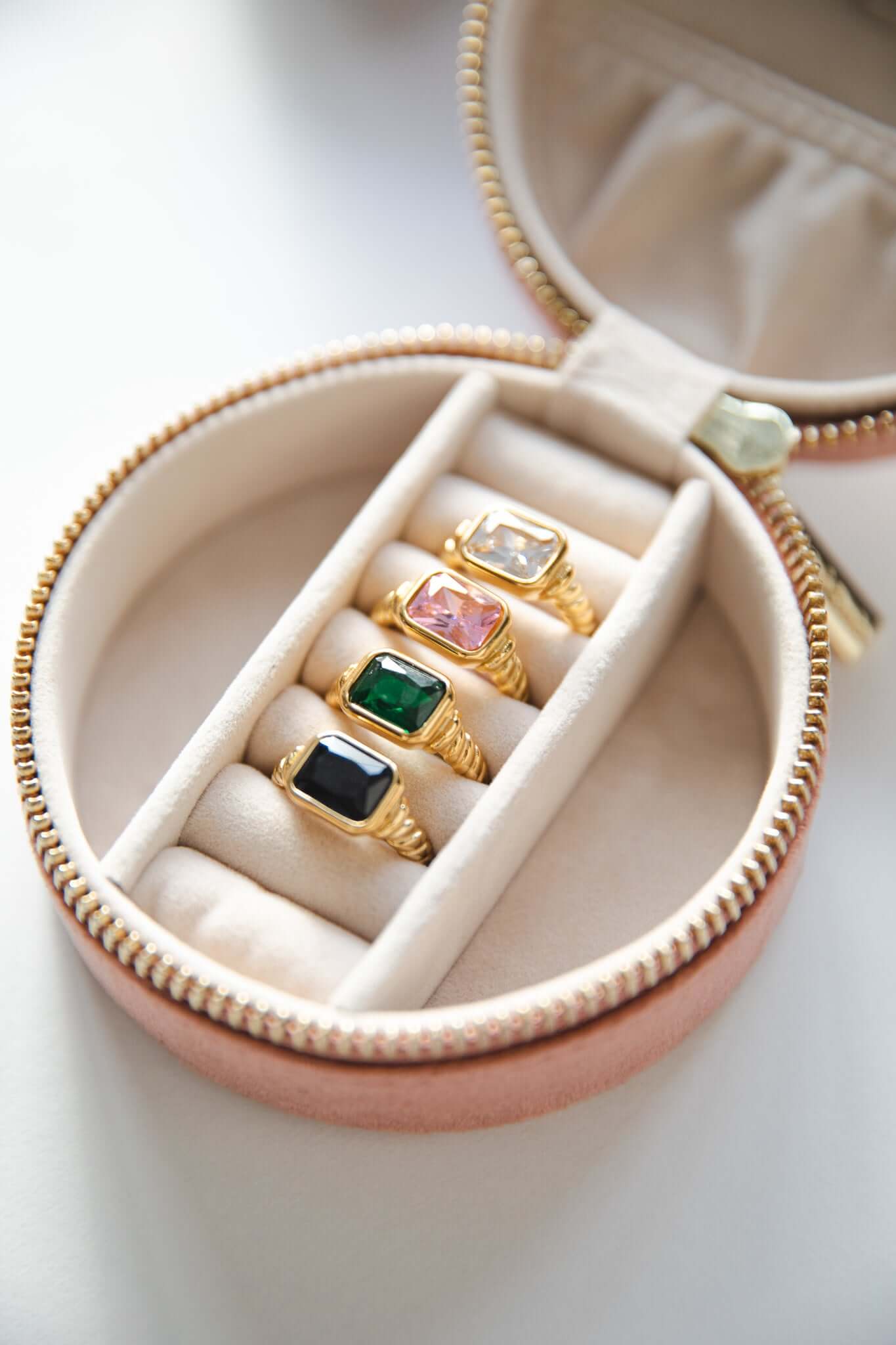 Vintage Vibes RING collection flatlay showing four twisted-band rings in a pink travel case, each set with a different colored stone.