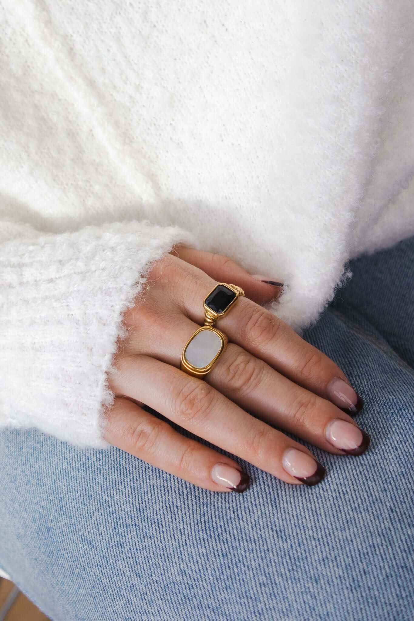 Vintage Vibes RING with black stone worn stacked with a separate oval white stone ring in a plain gold band, resting on denim.