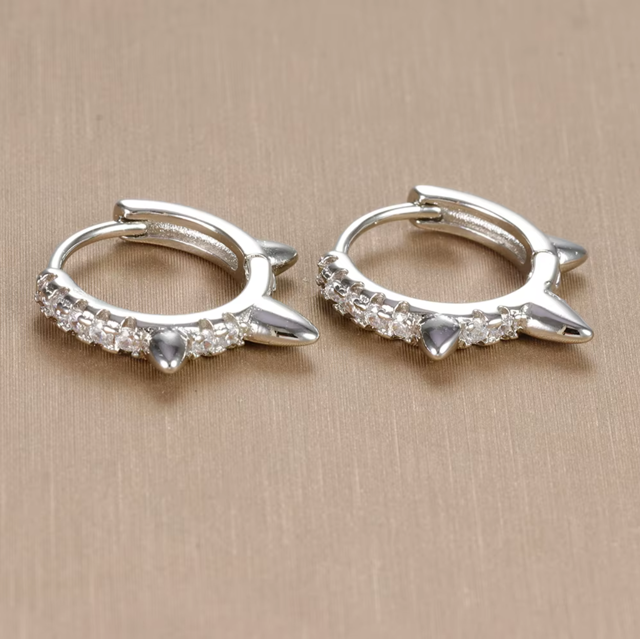Close-up of Wild Earrings in silver tone on beige fabric, showing the pave spike detail on the hoop.