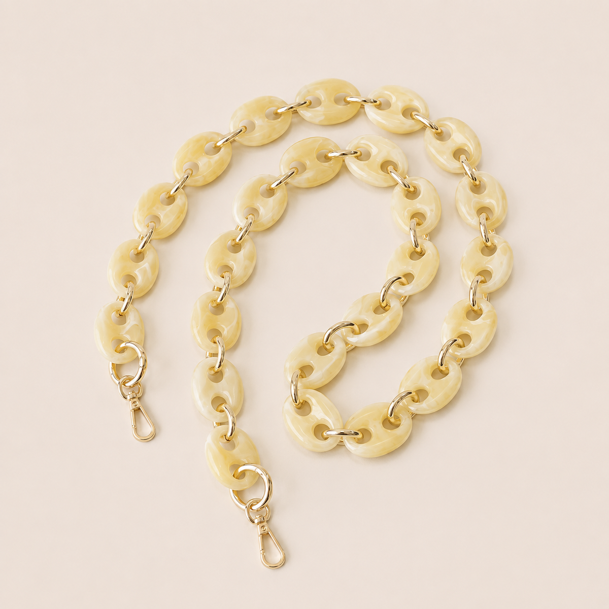 Folie à Trois Wilder long phone chain in ivory marbled puffed links with gold connectors, coiled on a cream background.