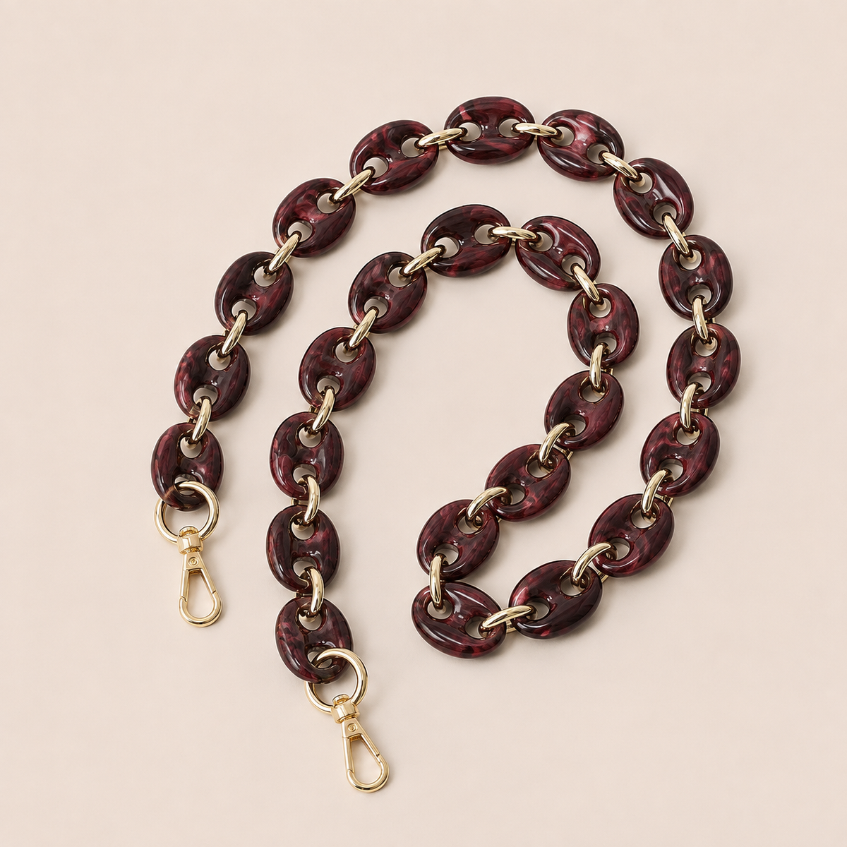 Folie à Trois Wilder long phone chain in wine red marbled puffed links with gold connectors, coiled on a cream background.