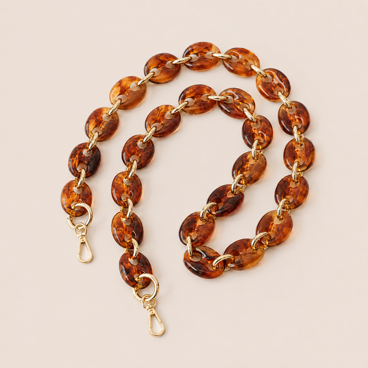 Folie à Trois Wilder long phone chain in amber tortoiseshell puffed links with gold connectors, coiled on a cream background.