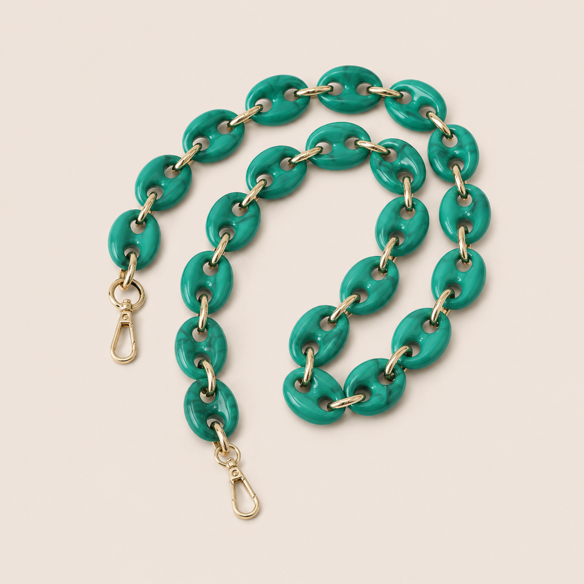 Folie à Trois Wilder long phone chain in teal green marbled puffed links with gold connectors, coiled on a cream background.