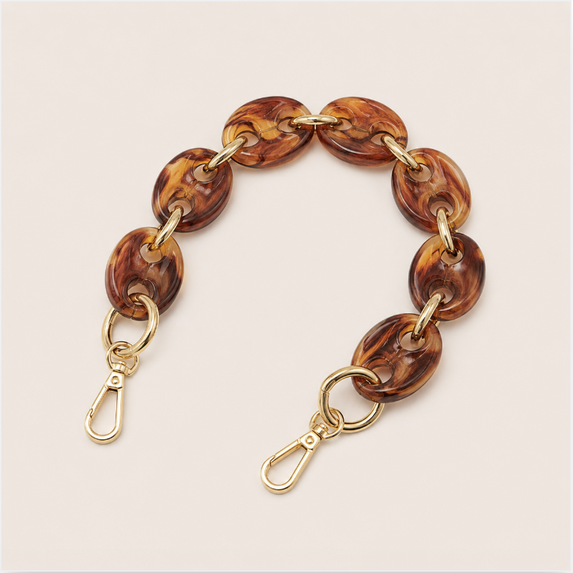 Folie à Trois Wilder short phone chain in amber tortoiseshell puffed links with gold connectors, laid flat on a cream background.