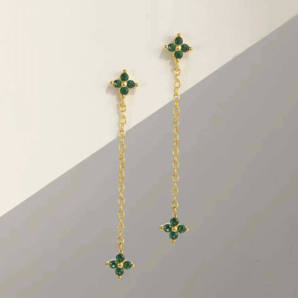 Zabbarra Earrings laid flat against a two-tone backdrop, showing the long chain with clover crystal studs at each end.