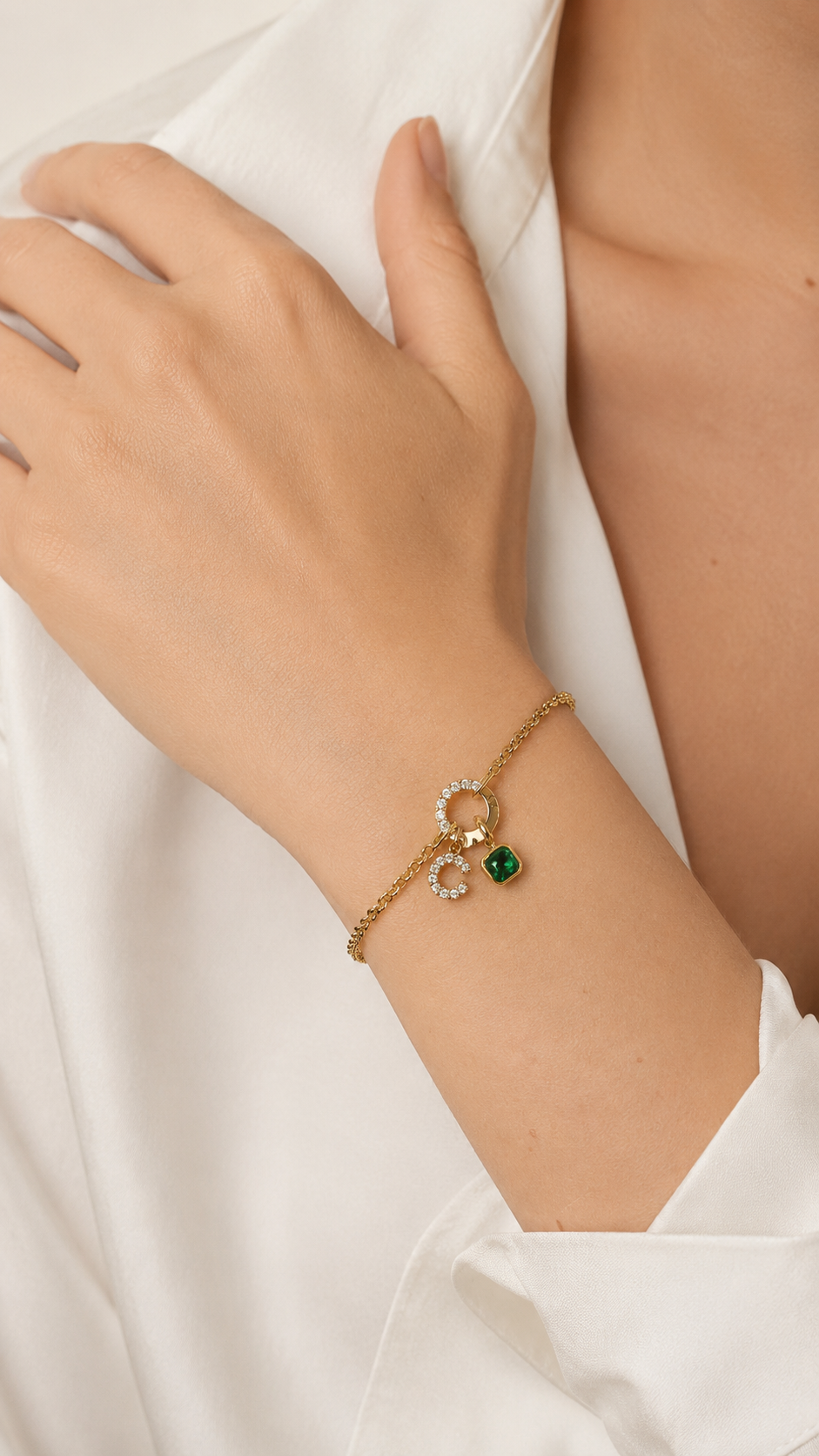 Zircon Charm BRACELET worn on the wrist, hand resting on a cream fabric, green zircon charm visible at the clasp.