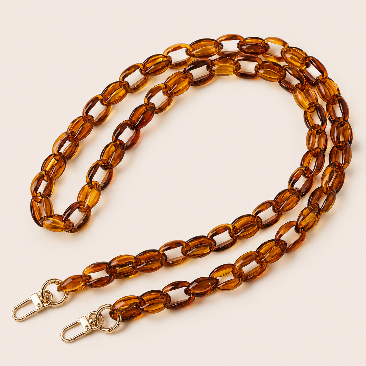 The Ember LONG PHONE CHAIN in amber transparent acrylic with gold-tone lobster clasp ends, coiled into a loop on a light beige background.