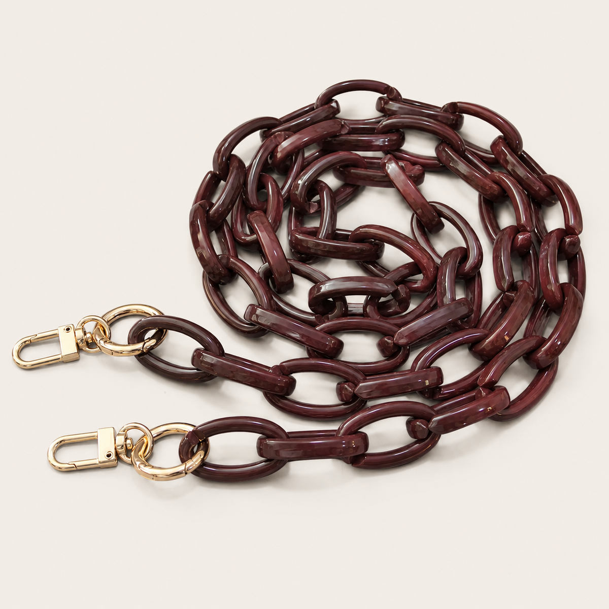 The Ember LONG PHONE CHAIN in deep burgundy acrylic with gold-tone lobster clasp ends, coiled into a loop on a light beige background.