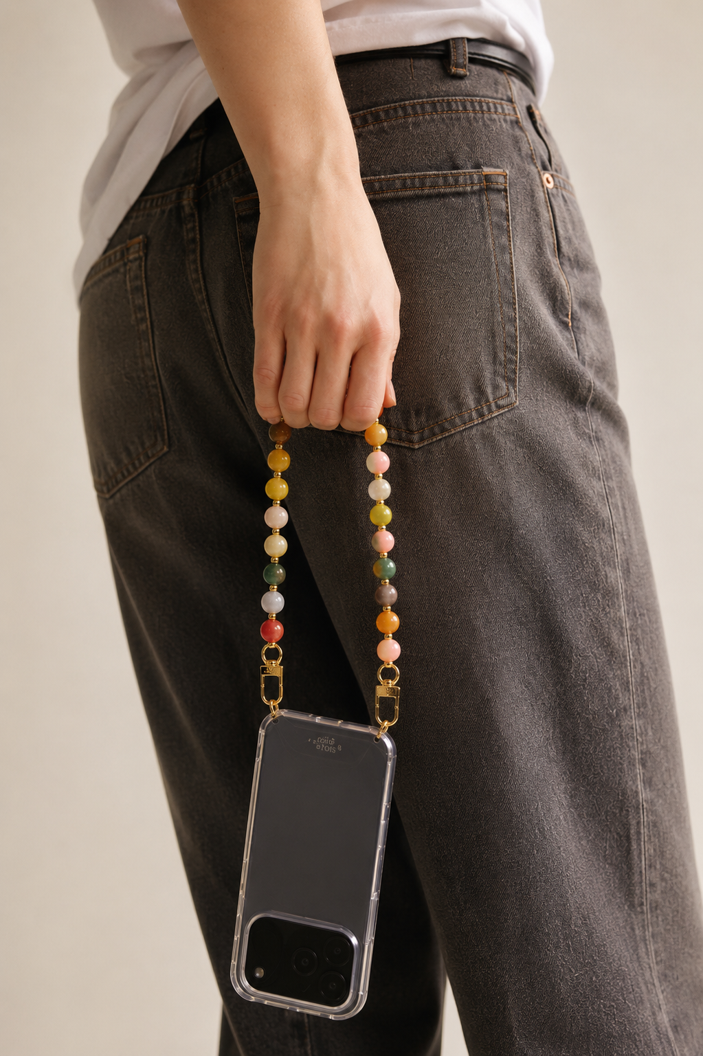 A model holds her phone in a black case attached to the pastel multicolor Sable PHONE CHAIN, styled against dark denim.