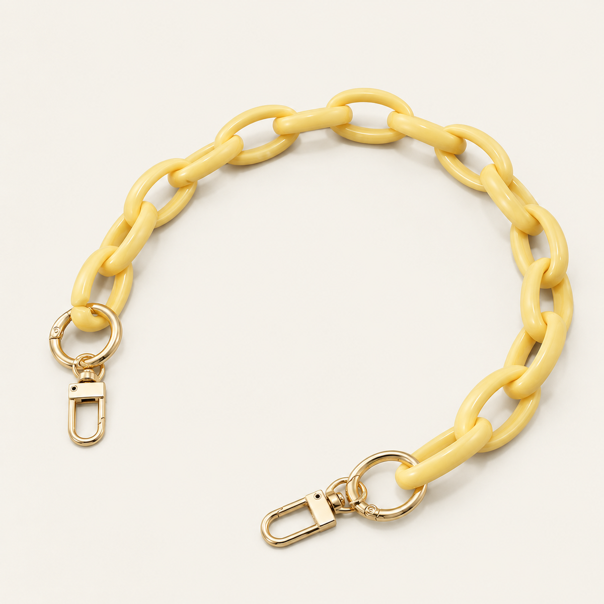 The Ember SHORT PHONE CHAIN in pale yellow acrylic with gold-tone lobster clasp ends, curved on a light beige background.