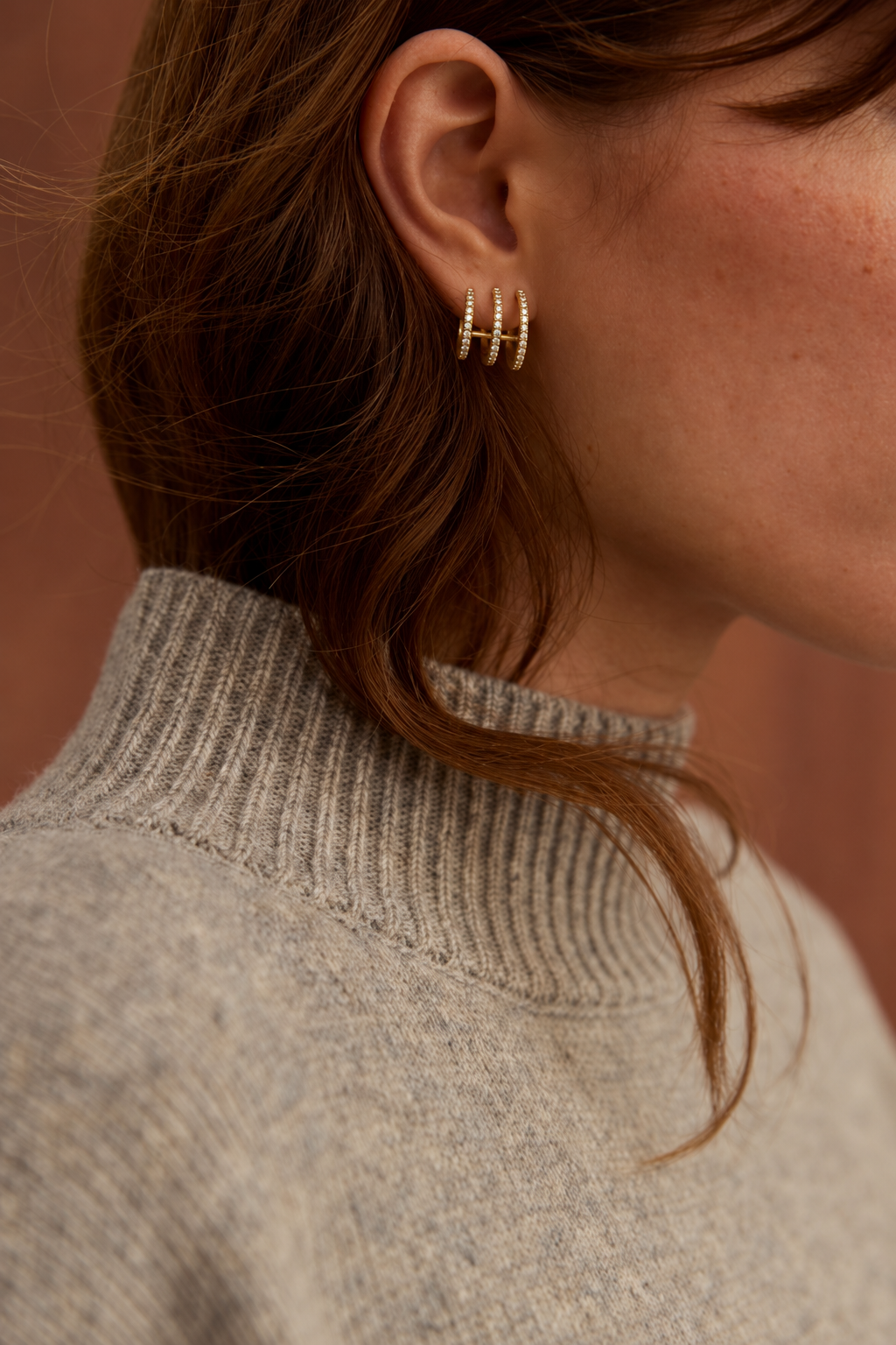 Close-up of gold Triad EARRINGS in the lobe, three pavé bands side by side on a model with brown hair.