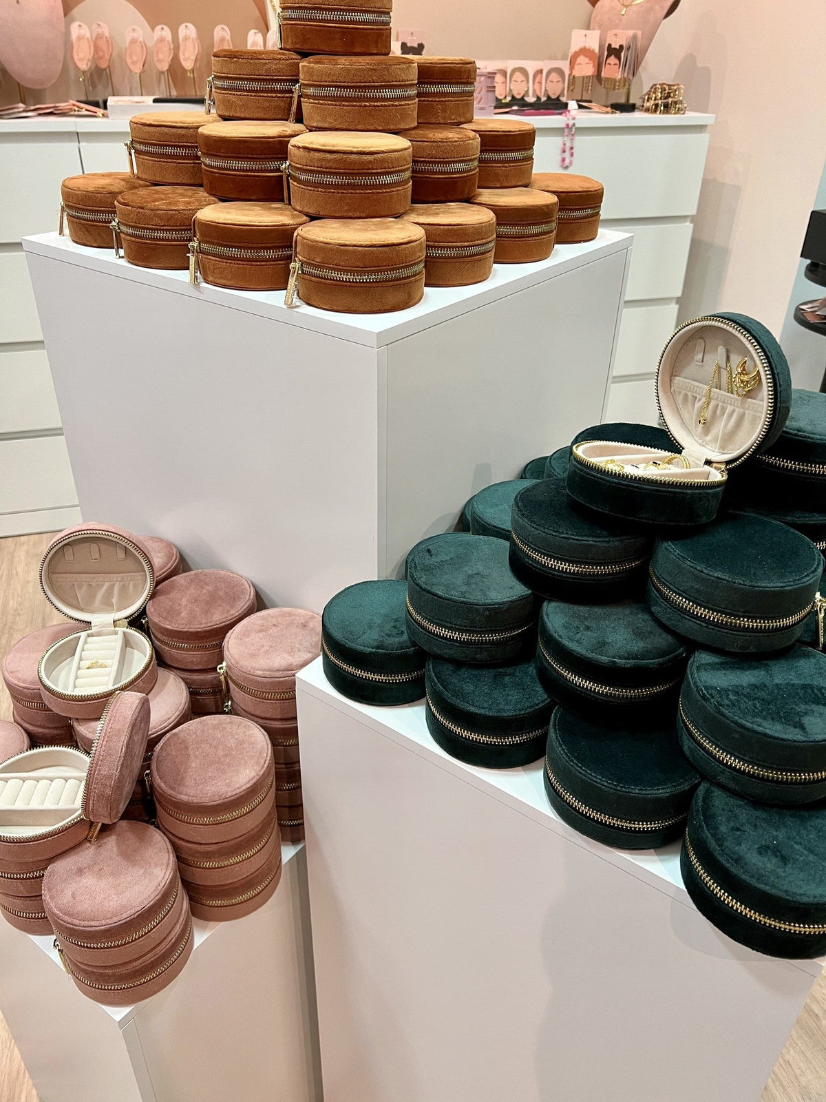 Stacks of round Travel Jewelry CASE pouches in cognac, blush pink and dark green velvet displayed on white plinths.