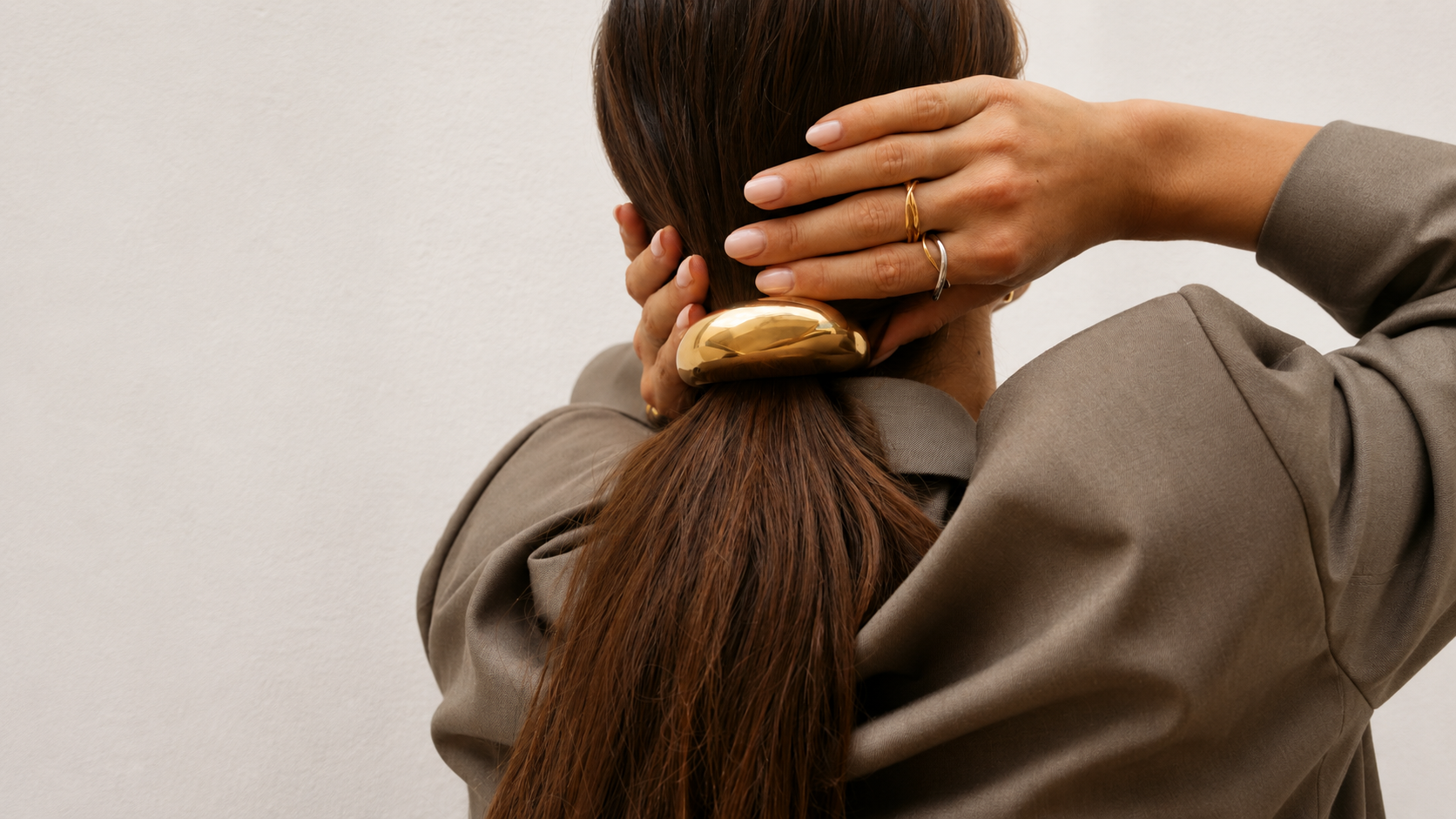 Back view of a woman in an olive jacket pinning her low bun with a gold hair clip.