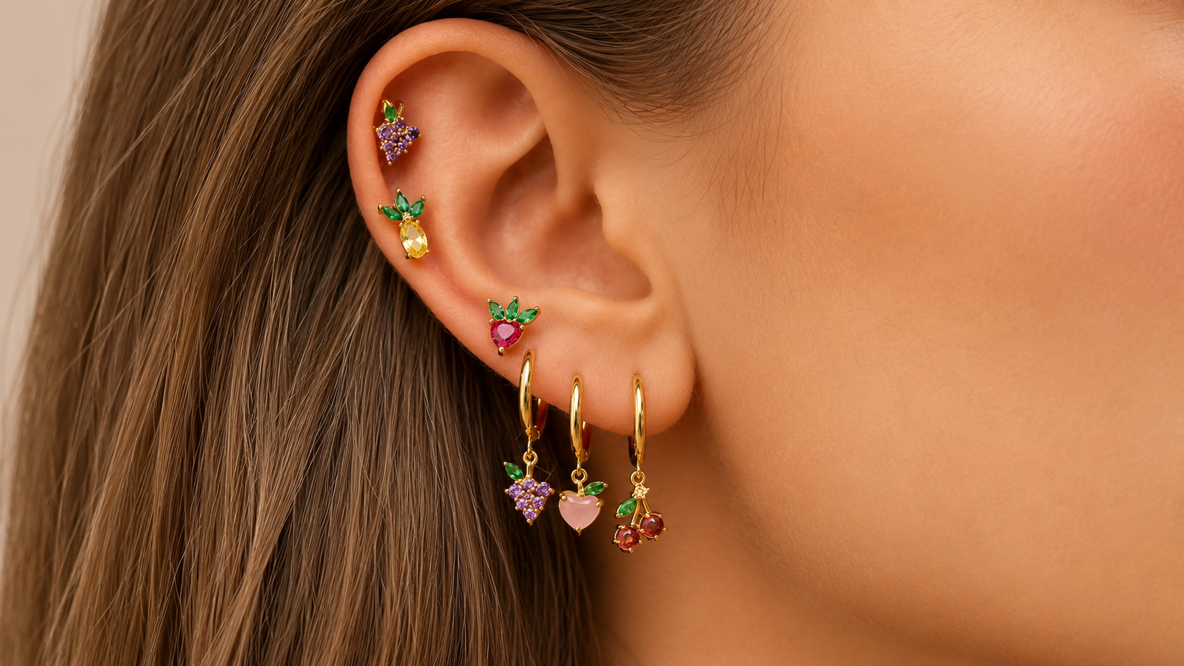 Close-up of a woman's ear stacked with small gold hoop earrings and ear cuffs featuring colorful heart-shaped charms.