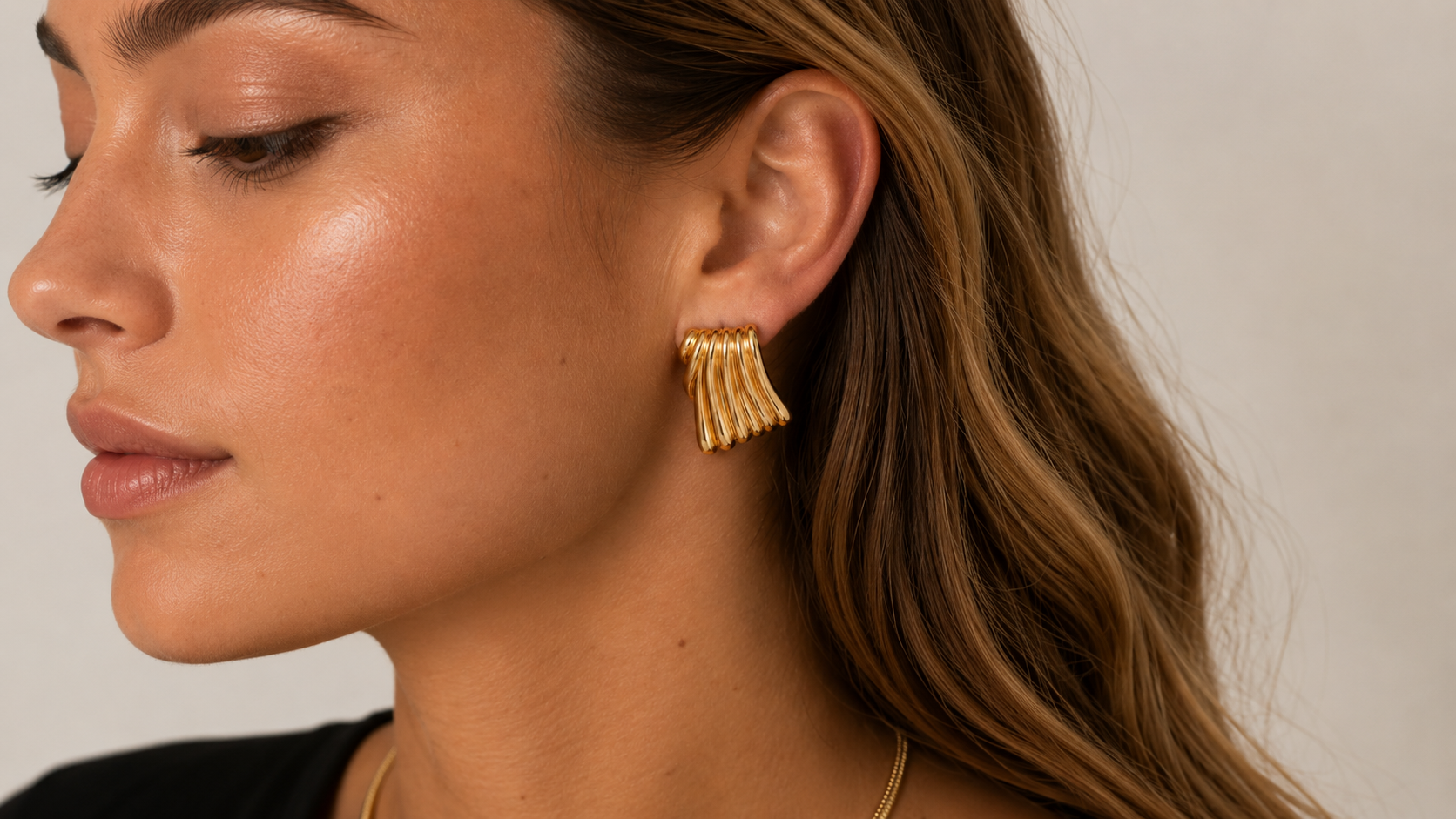 Side profile of a woman wearing a gold sunburst stud earring and a thin necklace.