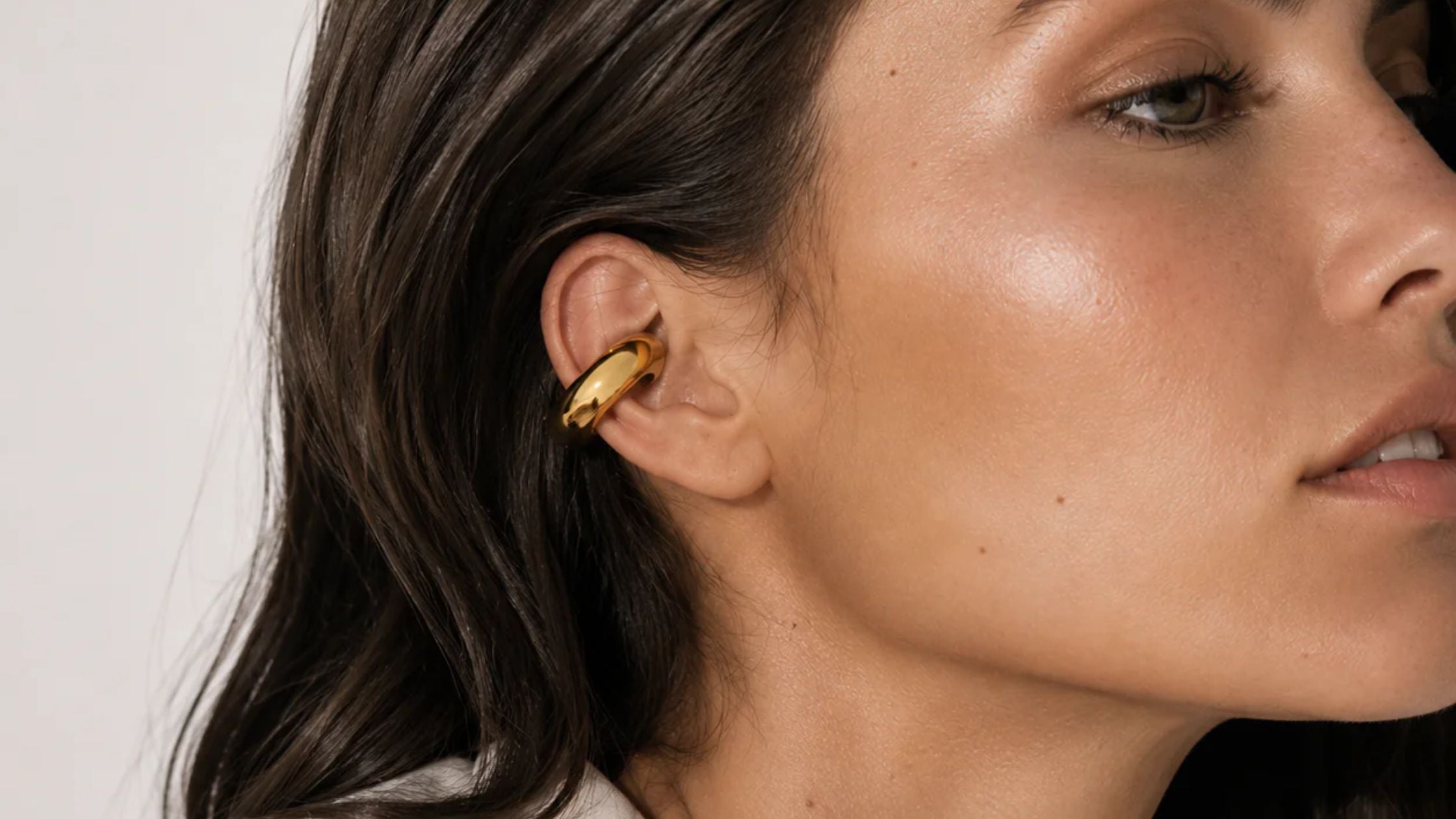 Close-up of a woman's ear wearing a gold ear cuff wrapped around the upper cartilage.