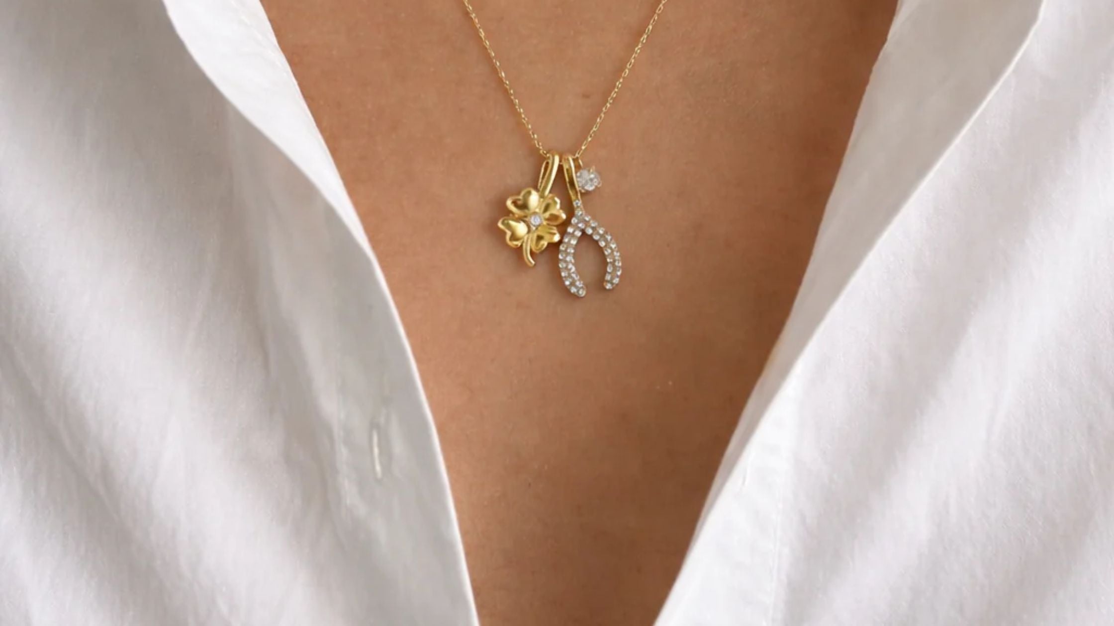 Close-up of a woman's collarbone in a white shirt, wearing layered gold necklaces with small charm pendants.