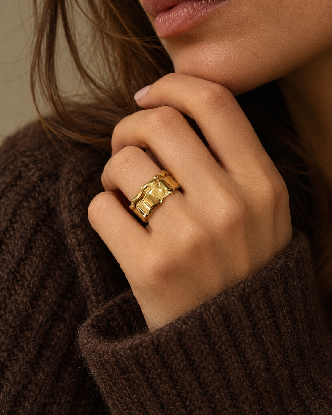 Model in a brown knit jumper wearing the wide, wavy gold Marée RING stacked on one finger.