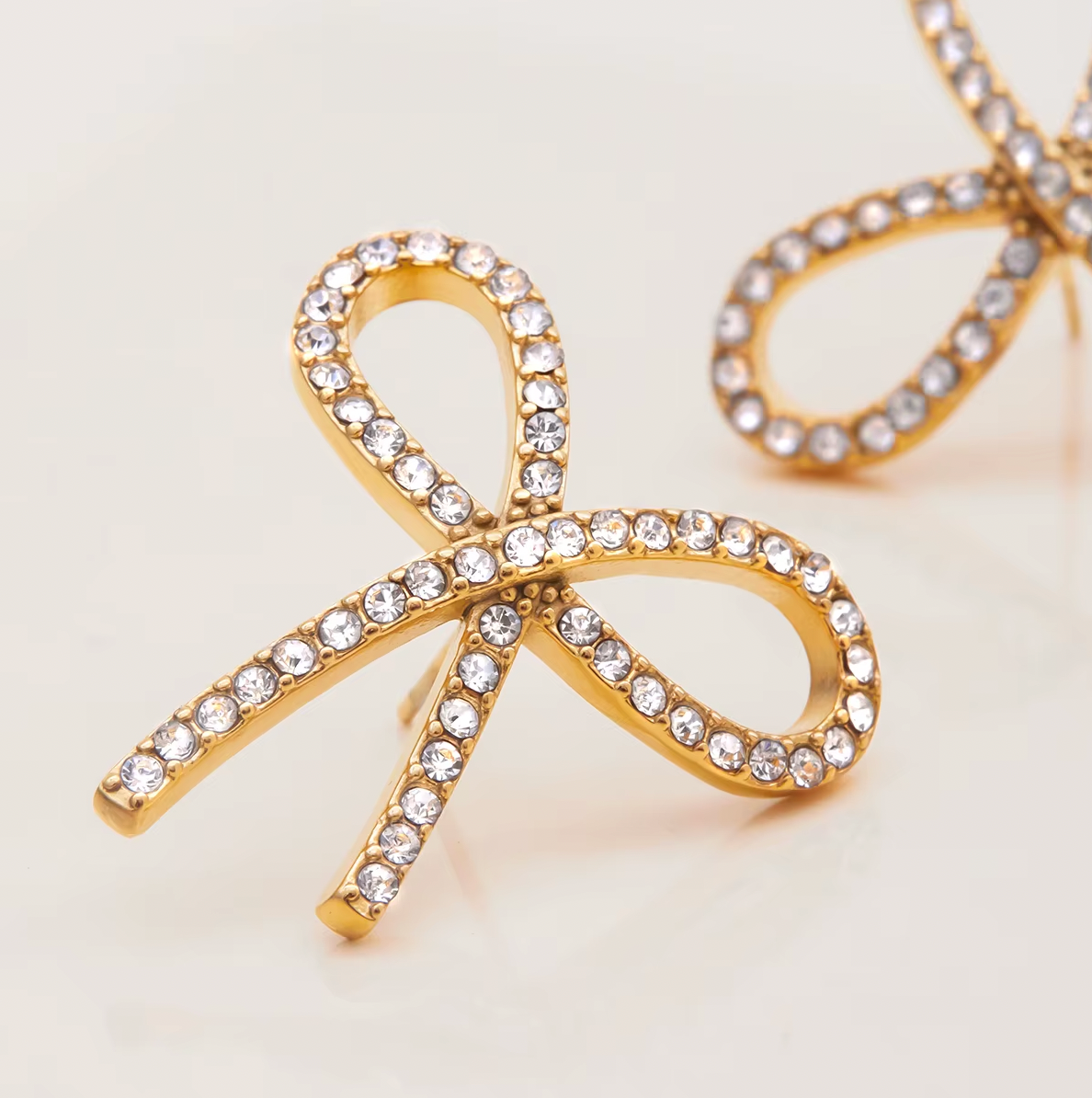 Gold-plated bow-shaped stud earrings embellished with clear crystal stones