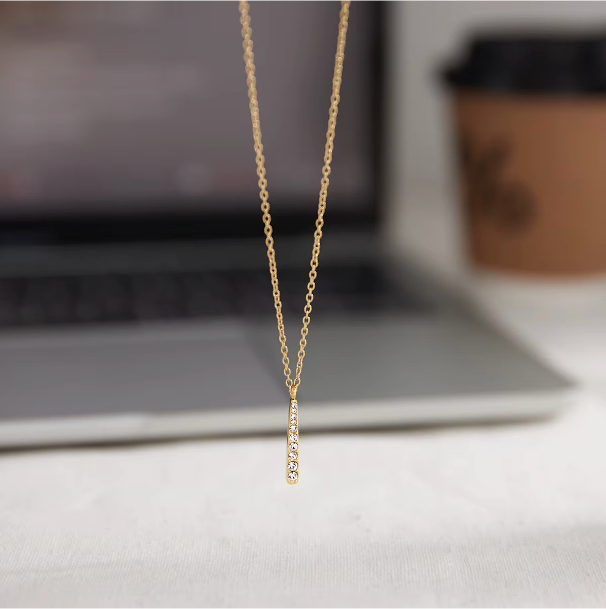 Gold-plated necklace with a fine chain and a slim vertical bar pendant set with clear crystal stones