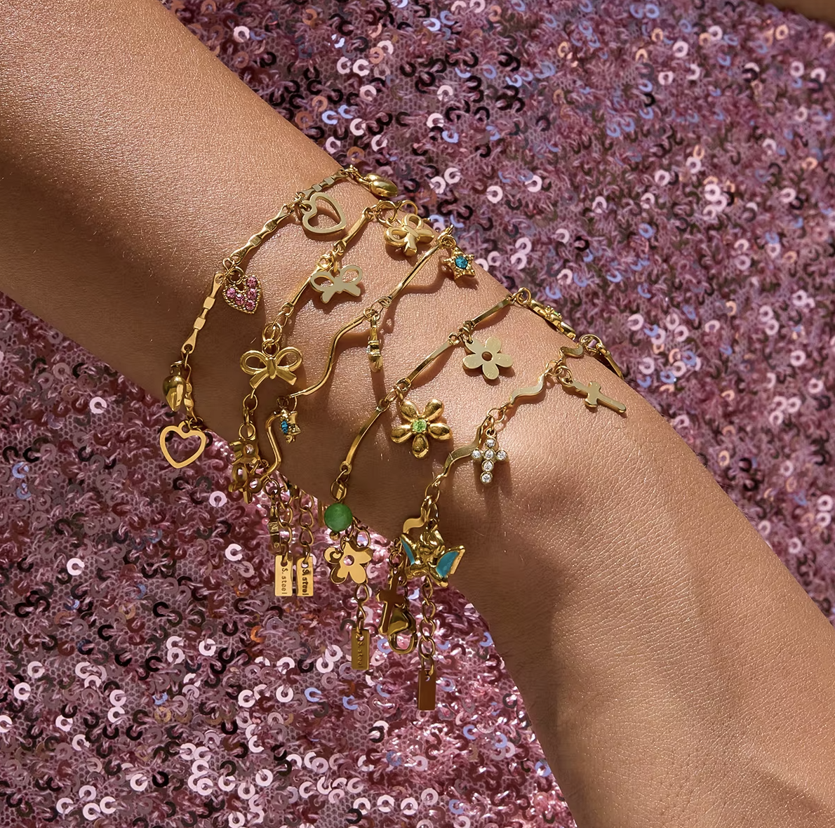 Gold-plated charm bracelet with multiple heart-shaped charms, including open hearts, polished gold hearts, and a pink crystal heart