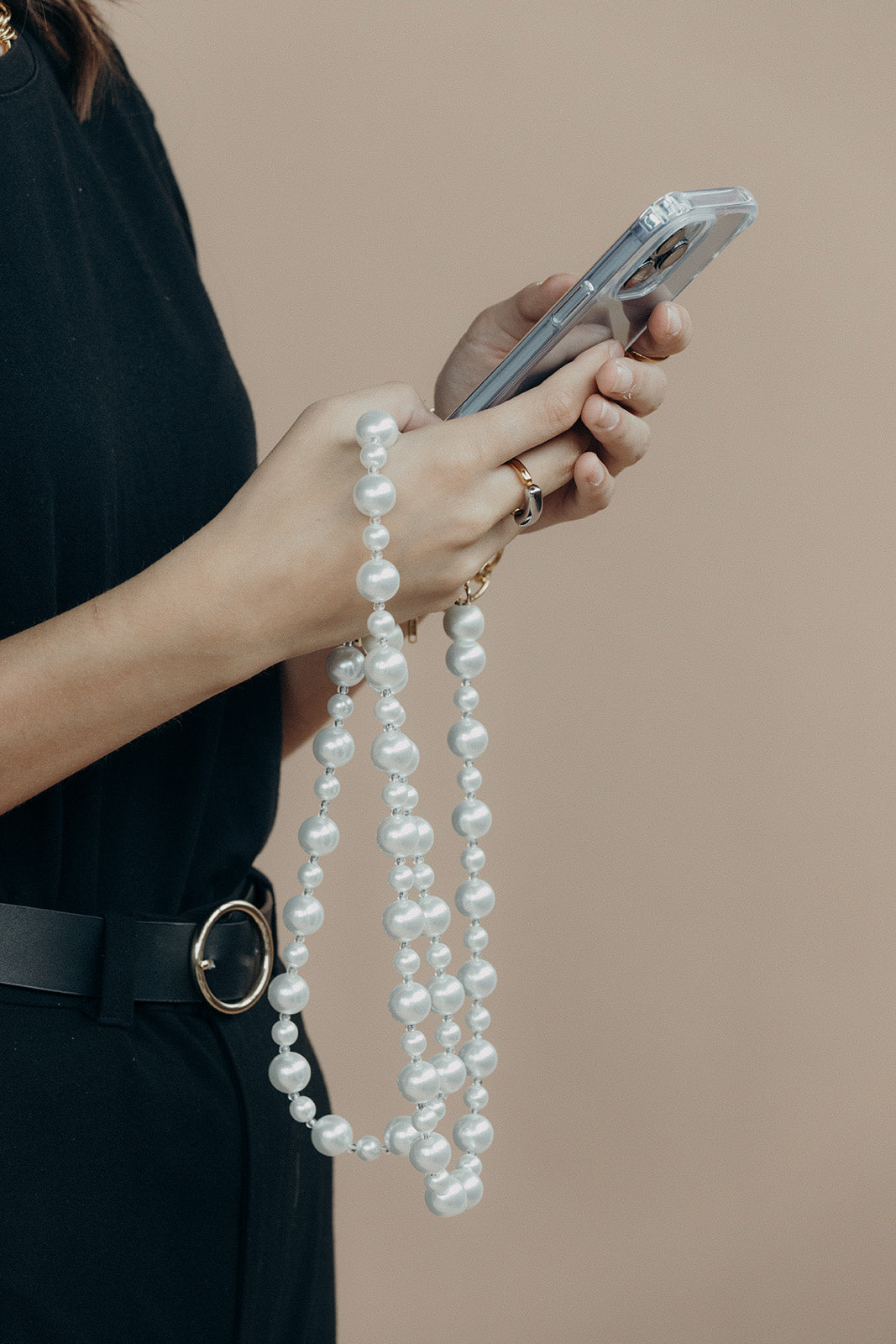 Model in black holding a phone with the Folie à Trois Adair Pearl wholesale phone chain draped over her hand.