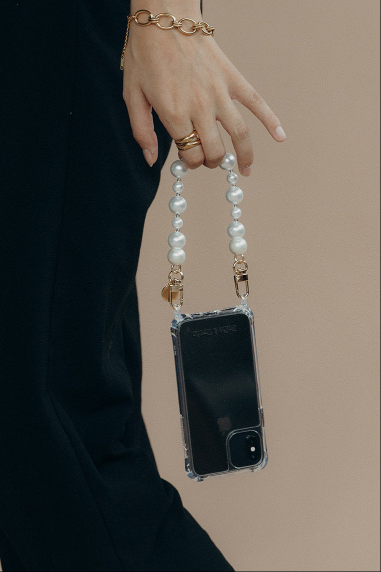 Model holding a clear phone case by the Folie à Trois Adair Pearl wholesale phone chain, paired with a gold chain bracelet.