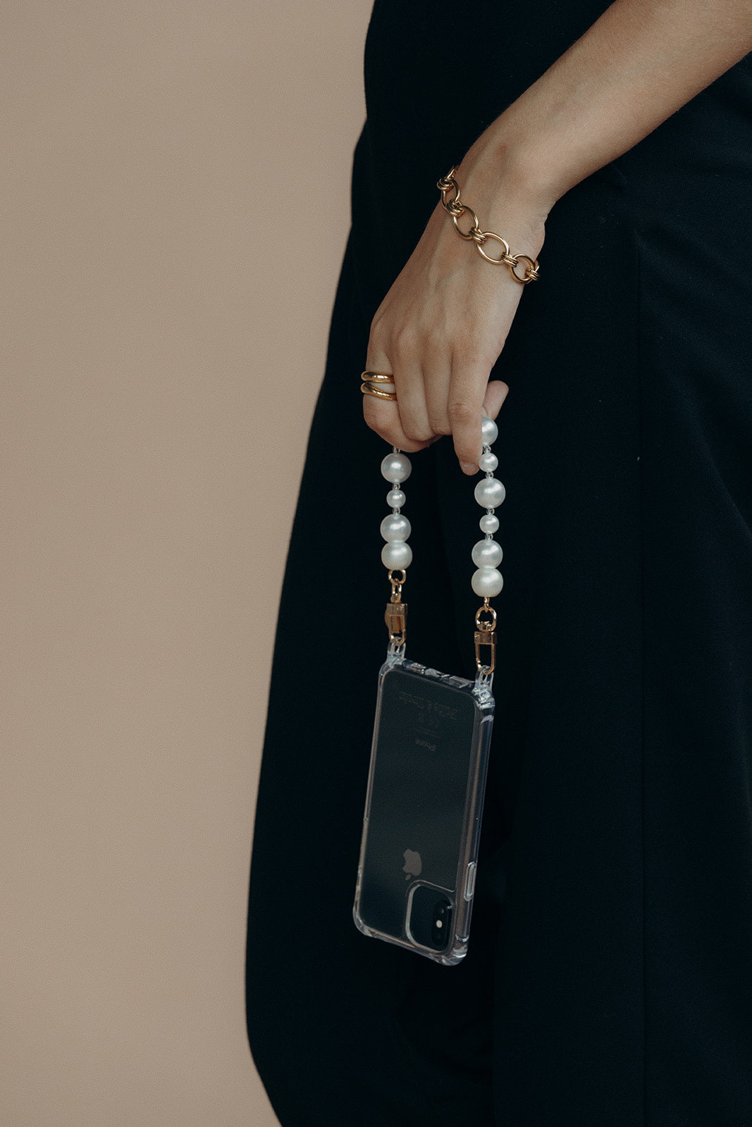 Close-up of a model's hand holding a phone in a clear case by the Folie à Trois Adair Pearl wholesale phone chain and gold clasps.