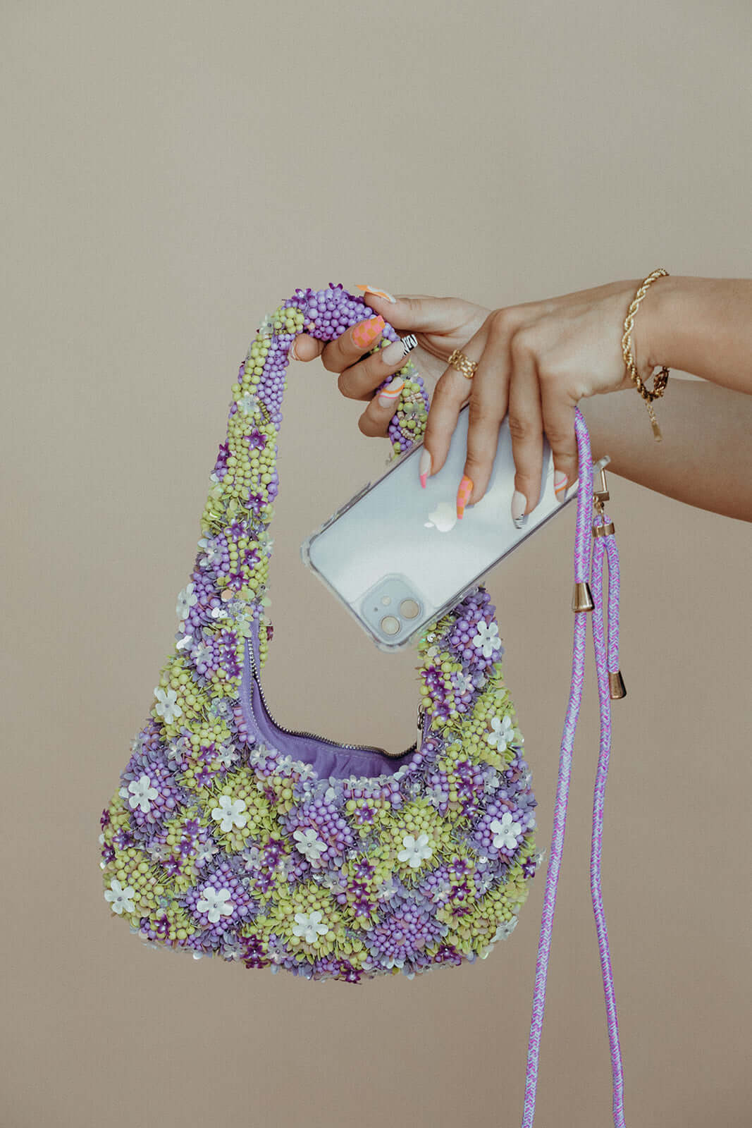 Hand holding a floral beaded shoulder bag with a lavender Aesthetic Colorful PHONE CORD attached to a phone case.