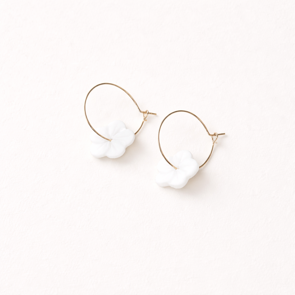 After Glow Earrings string a white flower-shaped bead onto a thin gold wire hoop for a light, airy look.