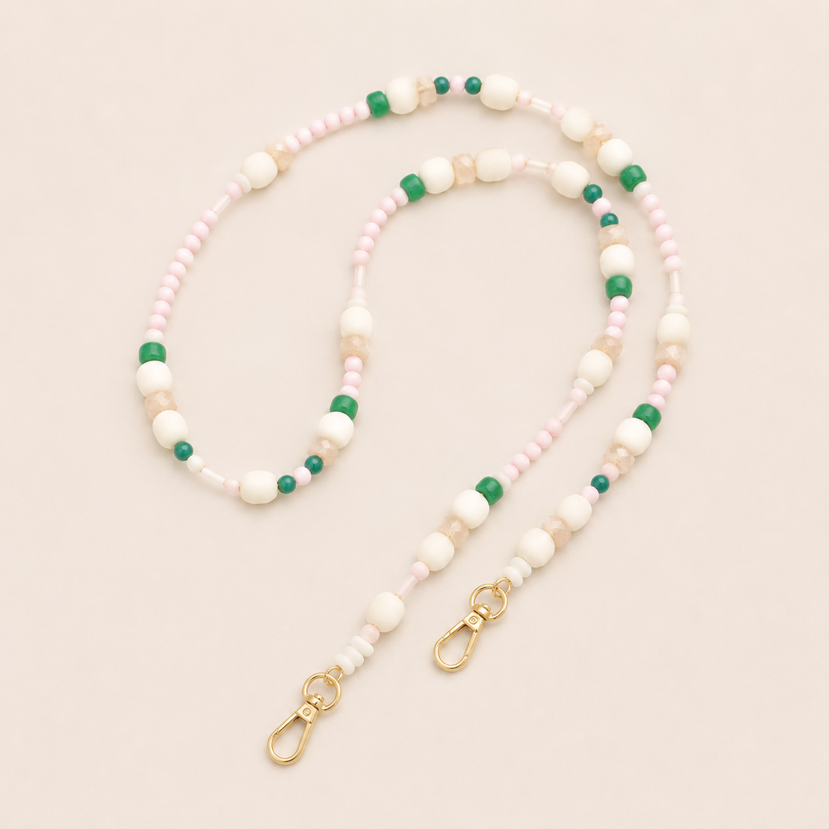 Folie à Trois Alder long phone chain in pink, cream, sand and green seed and round beads with gold lobster clasps, coiled on a cream background.