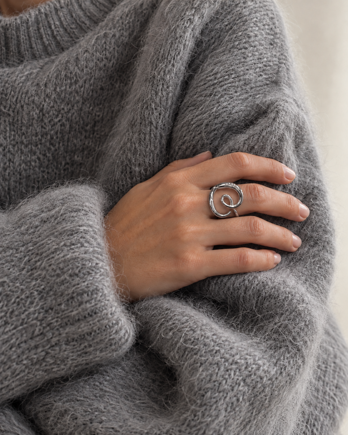 Arm crossed over a grey mohair sweater, hand wearing the silver-tone Amore RING curled into a heart — Folie à Trois wholesale