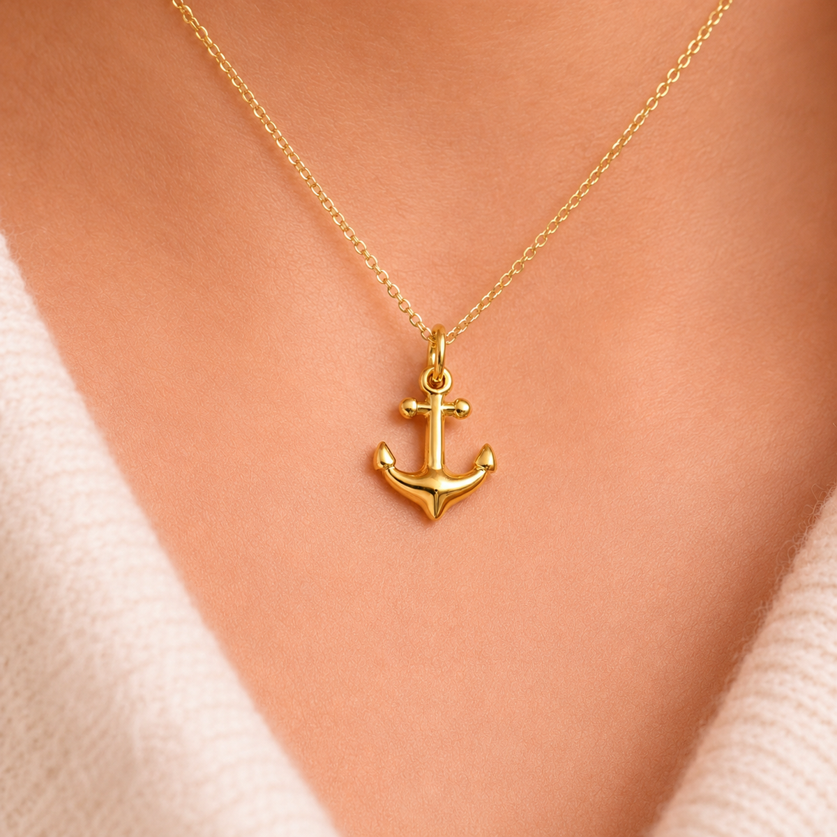 The Anchor CHARM worn on a fine gold chain at the neckline, styled with a cream sweater in close-up light.