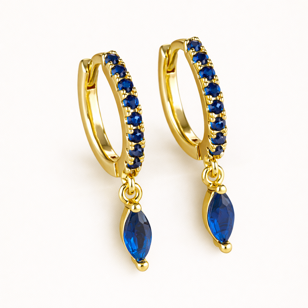 Anette Earrings in gold with sapphire-blue crystals, the pave huggie hoop dropping a marquise-cut blue charm.