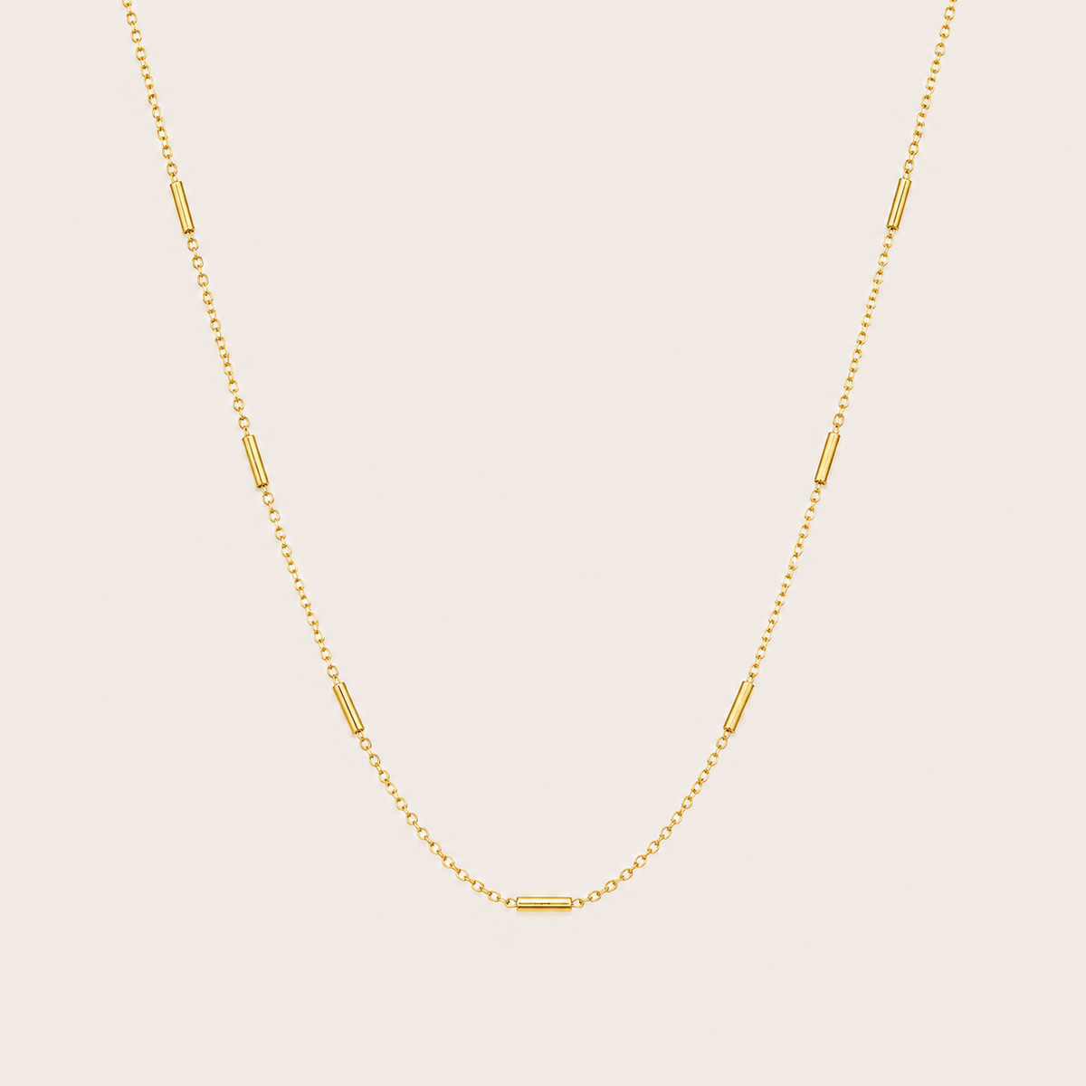 Gold chain necklace with small tube station beads spaced along the length, the Asta NECKLACE, shown in a close-up studio shot.