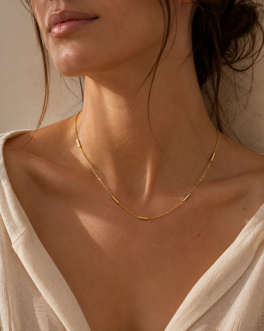A model wears the gold Asta NECKLACE, a delicate chain necklace with small tube station beads, layered close to the neckline.
