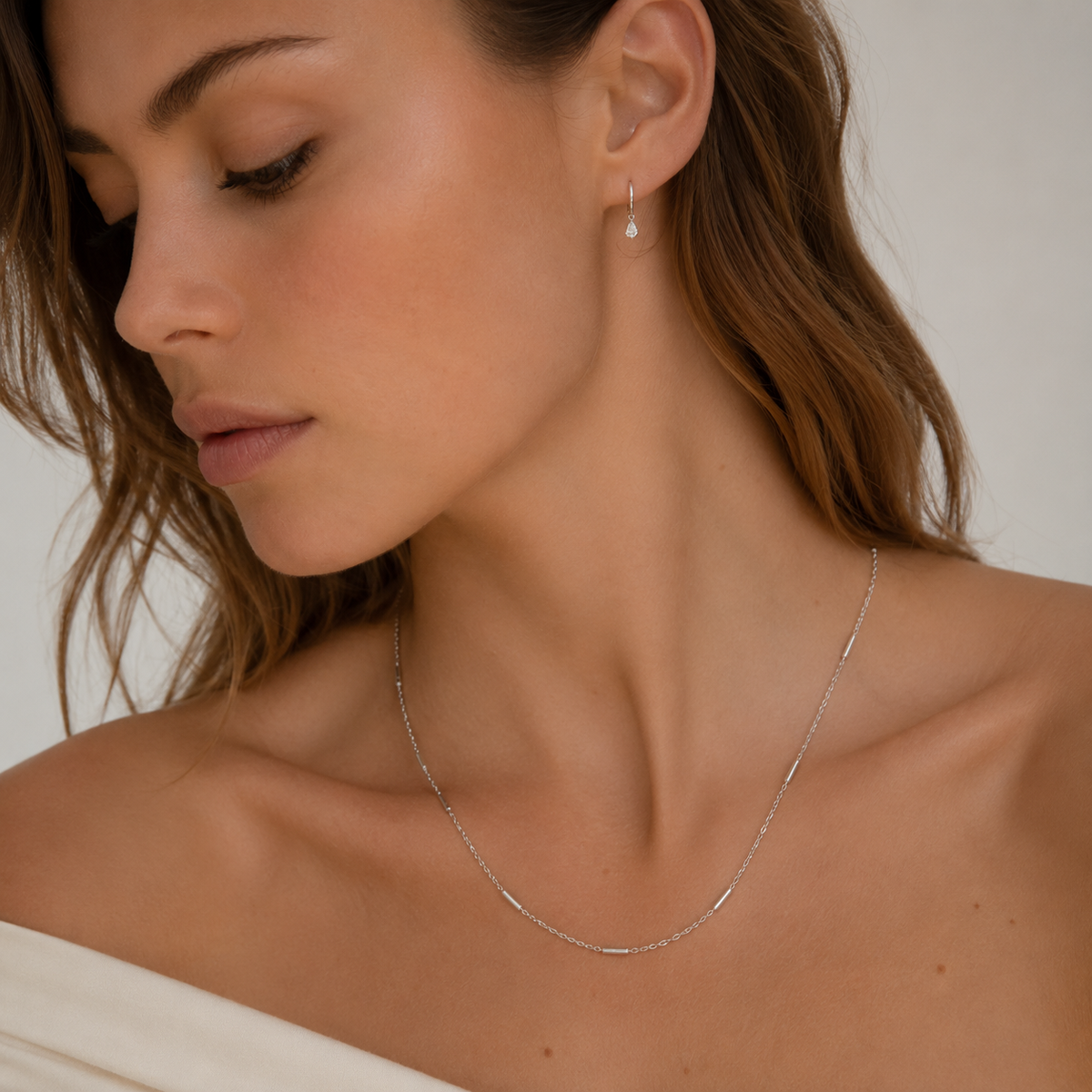 A model wears the silver Asta NECKLACE close to the neckline, paired with a matching teardrop earring.